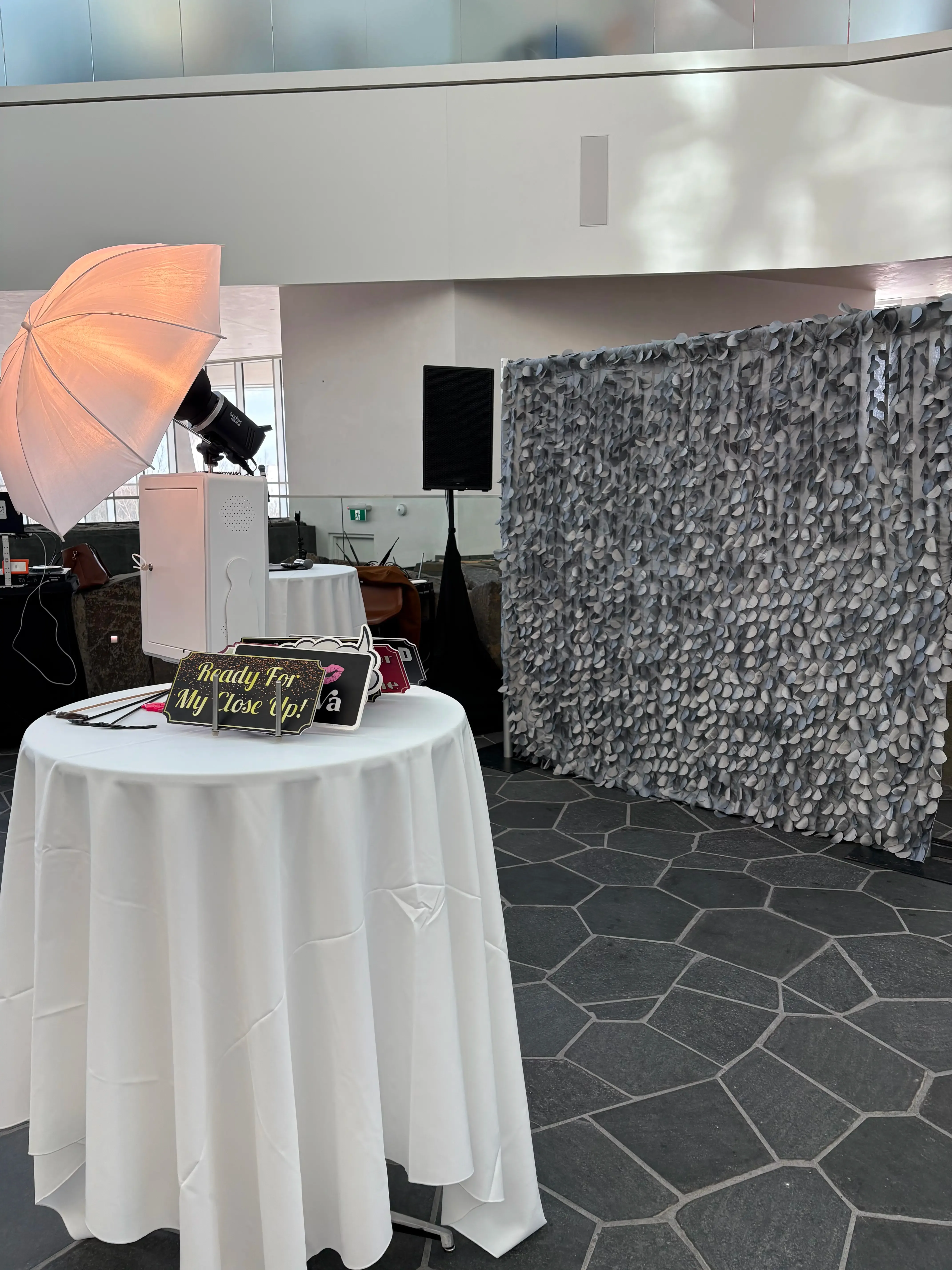 A photo booth with a 'Ready for my close up!' sign, set up against a lush leafy backdrop wall at a modern event venue