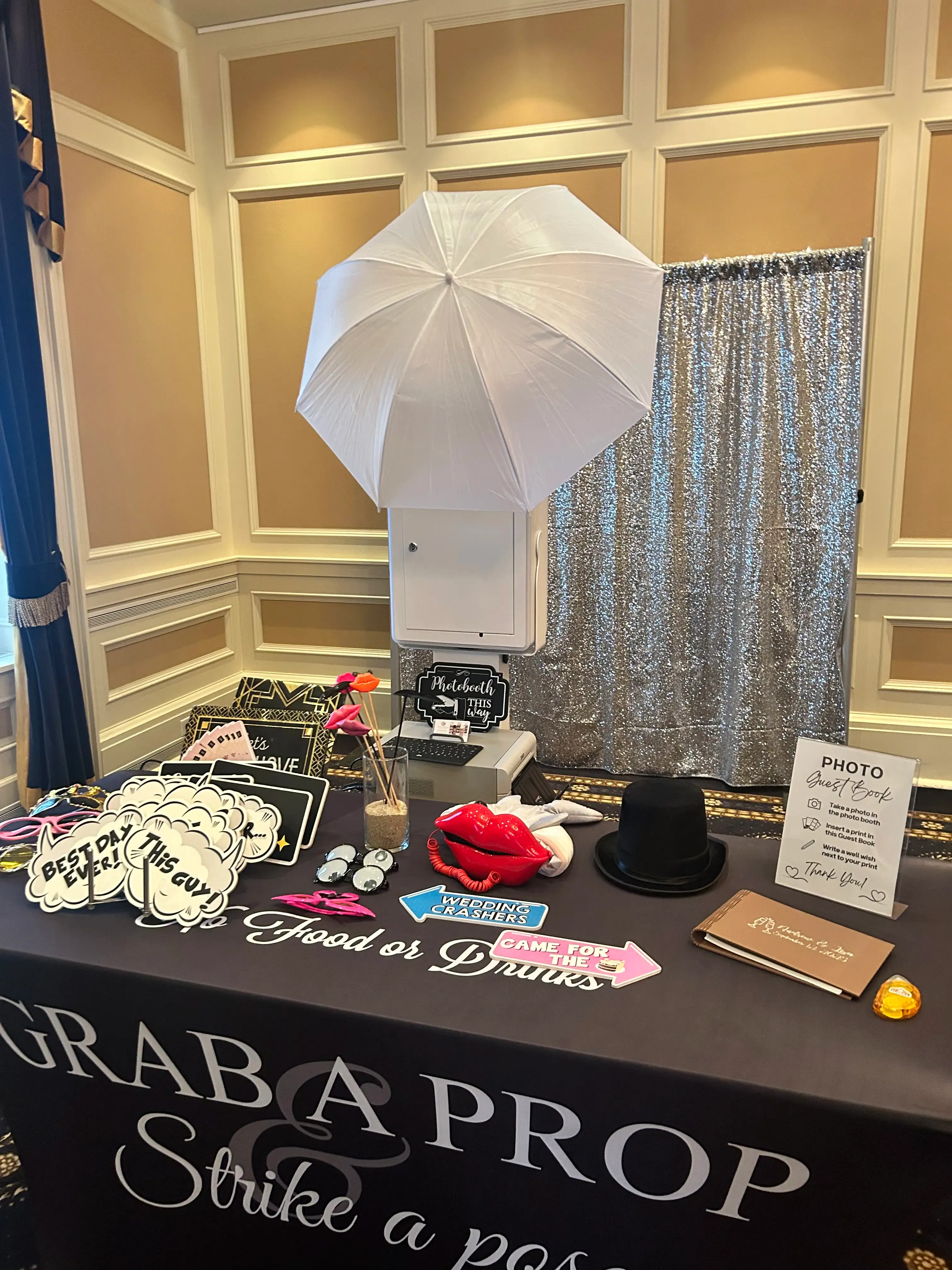 A sleek open-air photo booth with a 'strike a pose' props table, set up beautifully at an elegant wedding venue