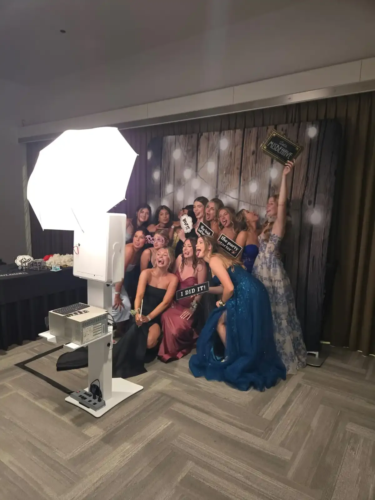 An excited group of guests cheering with props in front of an open-air photo booth experience