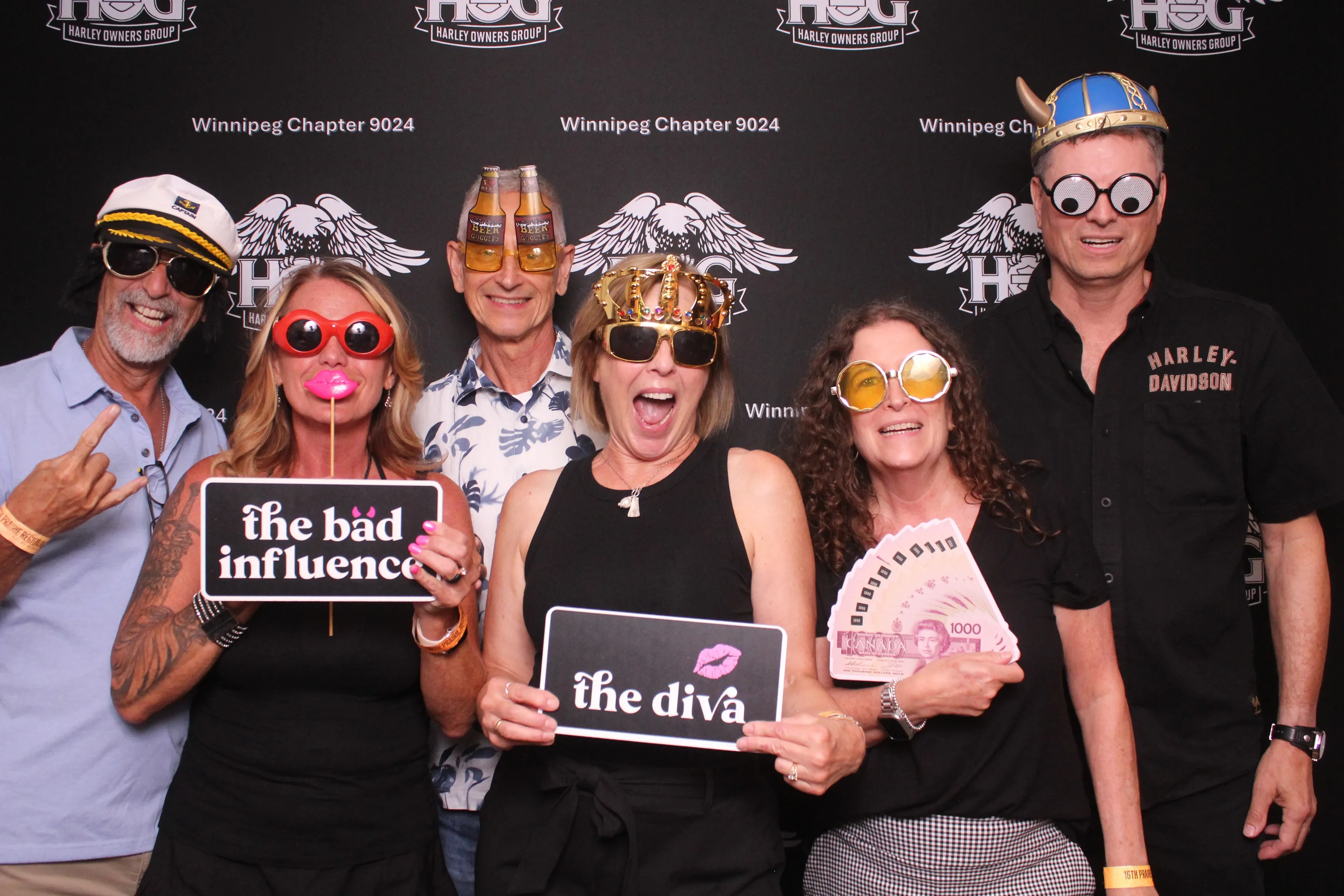 Guests striking fun poses with props in front of a custom-branded Harley Owners Group