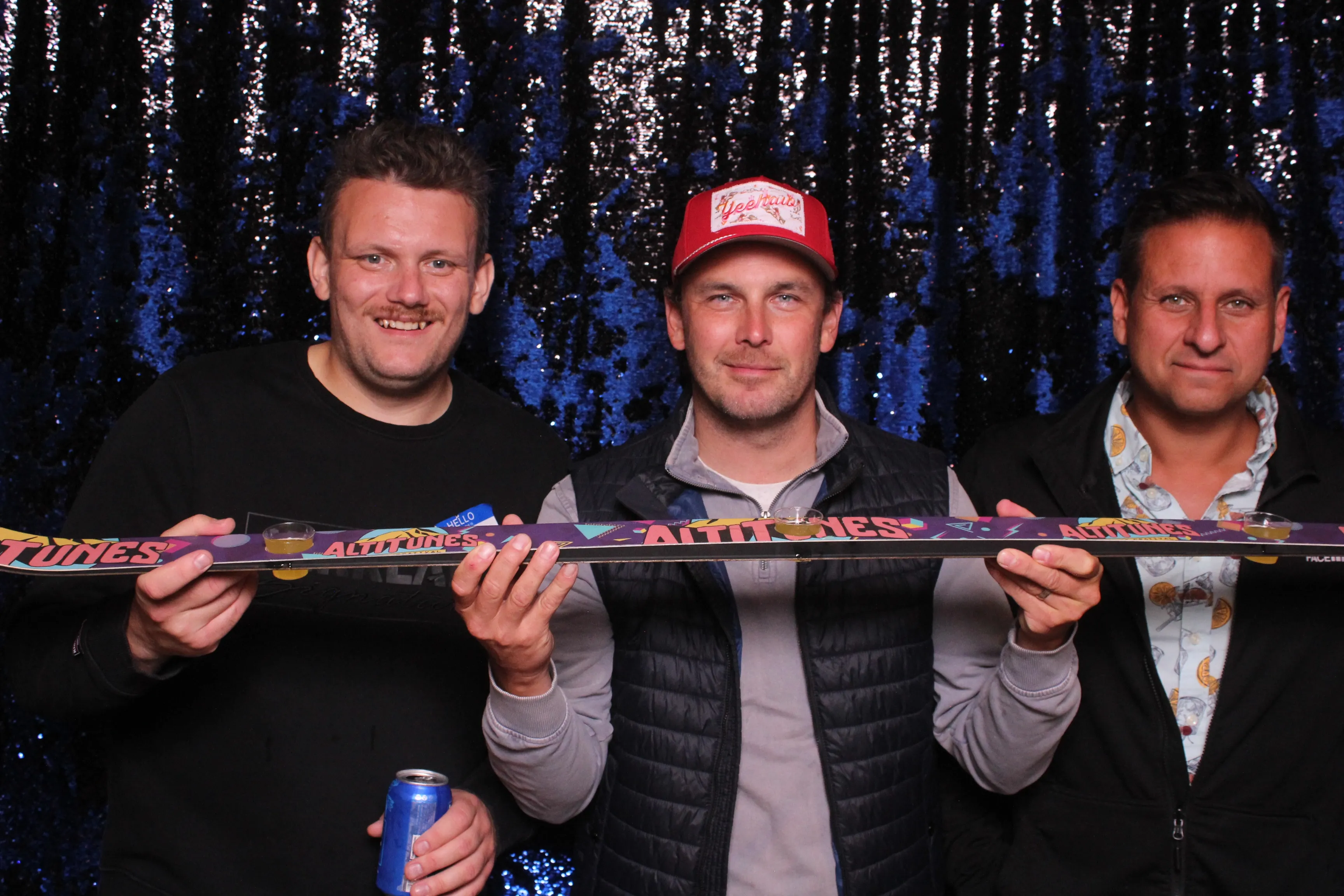 Friends raising a toast with a shot ski in front of a dark sequin backdrop