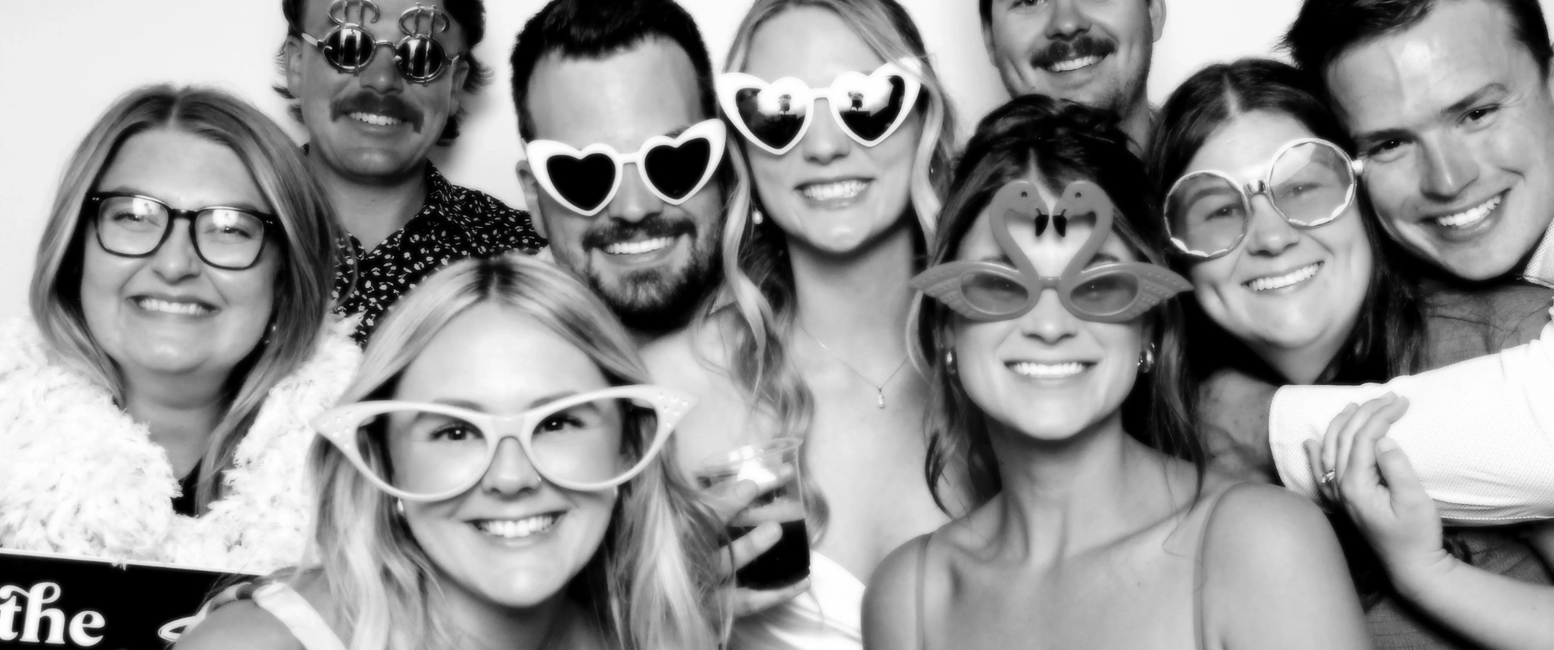 A wide black-and-white group shot of guests grinning with oversized fun props
