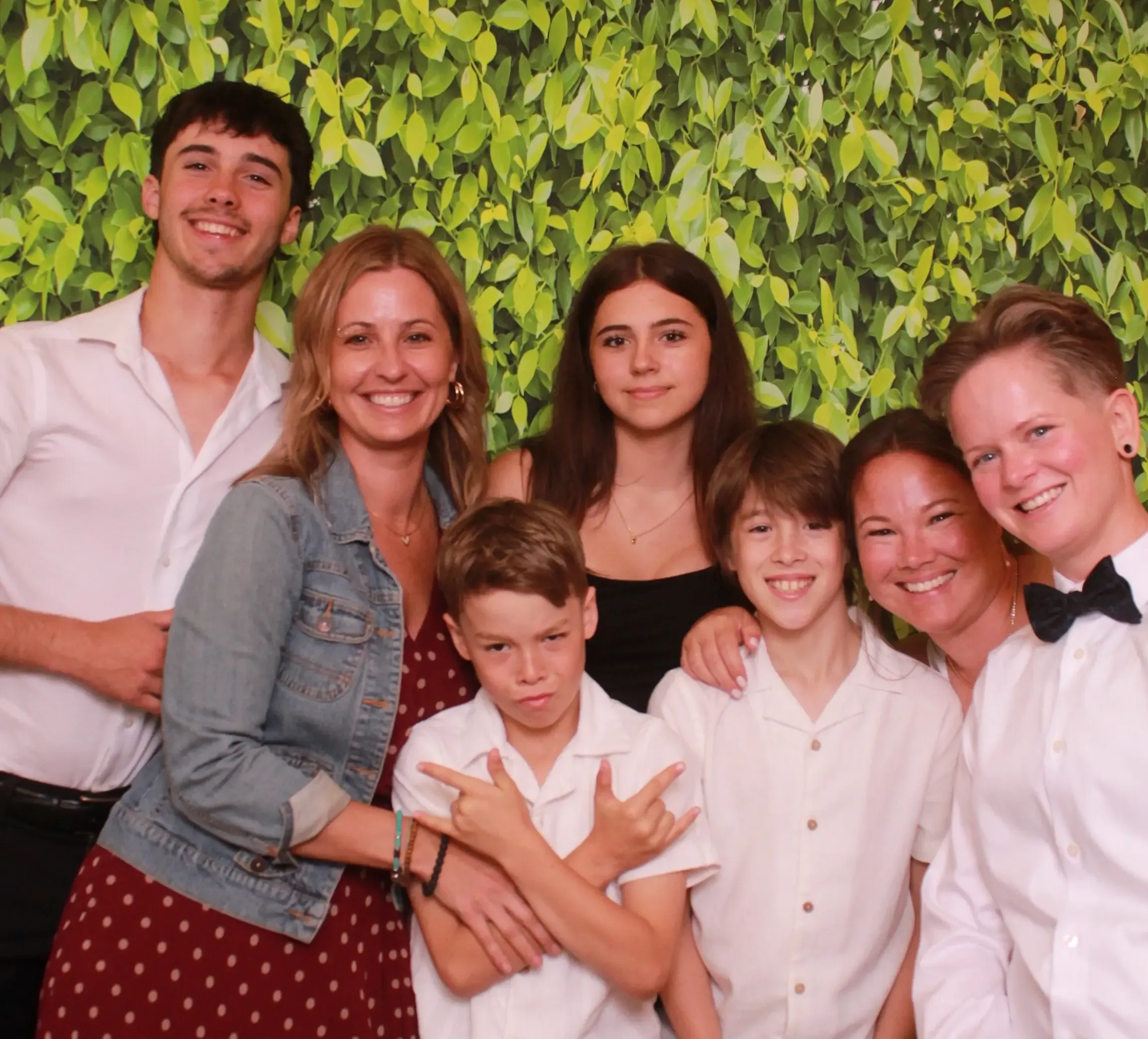 Friends and family of all ages posing together in front of a lush green-leaf backdrop